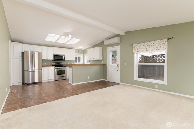 kitchen with lofted ceiling with skylight, appliances with stainless steel finishes, dark carpet, dark tile patterned floors, and white cabinetry