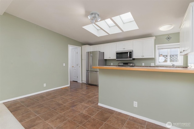 kitchen with vaulted ceiling with skylight, baseboards, white cabinets, a peninsula, and stainless steel appliances