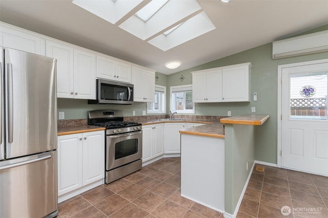 kitchen featuring stainless steel appliances, a wall mounted AC, lofted ceiling with skylight, white cabinetry, and a peninsula