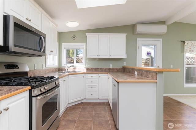 kitchen with a peninsula, a sink, appliances with stainless steel finishes, a wall mounted AC, and lofted ceiling with skylight