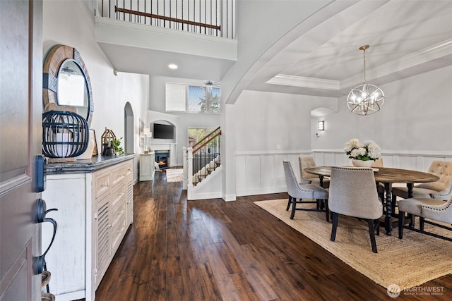 dining area with a warm lit fireplace, dark wood-type flooring, a wainscoted wall, and ornamental molding