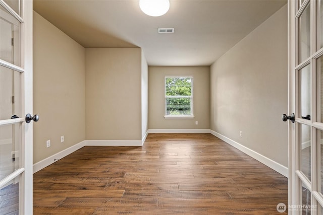 empty room featuring dark wood-type flooring, french doors, visible vents, and baseboards