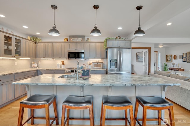 kitchen with an island with sink, appliances with stainless steel finishes, sink, and hanging light fixtures