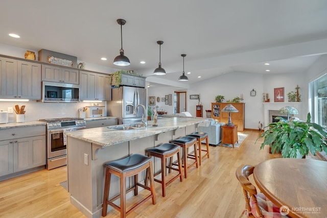 kitchen featuring sink, an island with sink, pendant lighting, stainless steel appliances, and light stone countertops