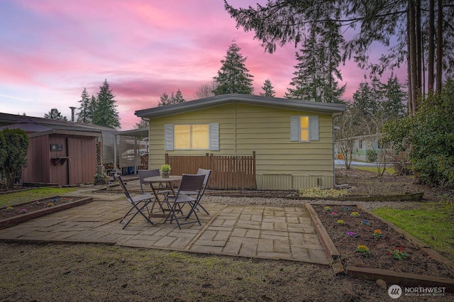 back house at dusk featuring a patio area and a storage unit