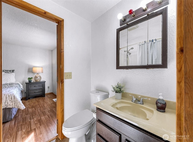 bathroom featuring a textured wall, toilet, a textured ceiling, vanity, and wood finished floors