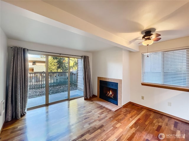 unfurnished living room with hardwood / wood-style flooring, ceiling fan, a fireplace, and beam ceiling