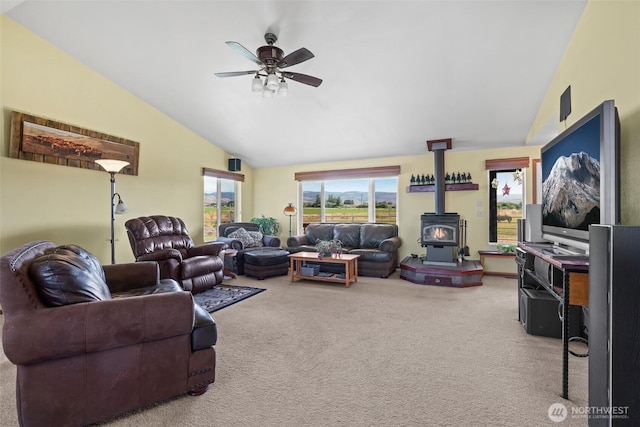 living area with vaulted ceiling, carpet flooring, a wood stove, and a ceiling fan