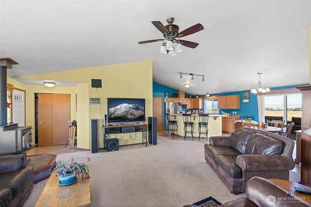 living room with light carpet, a wood stove, rail lighting, vaulted ceiling, and ceiling fan with notable chandelier