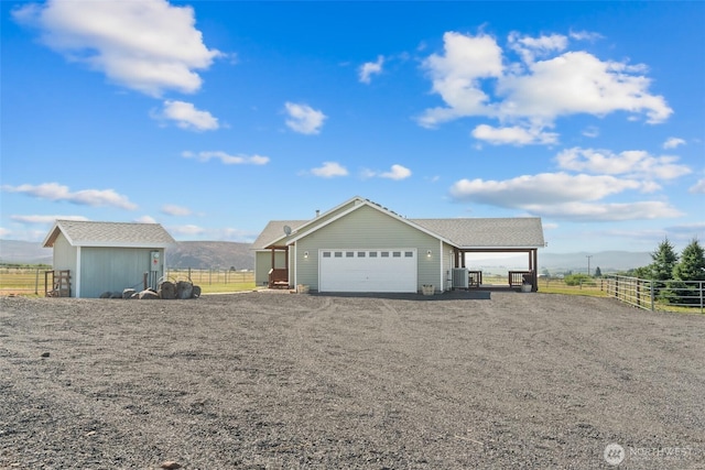 view of front of house with central AC unit, a rural view, gravel driveway, an outdoor structure, and a mountain view