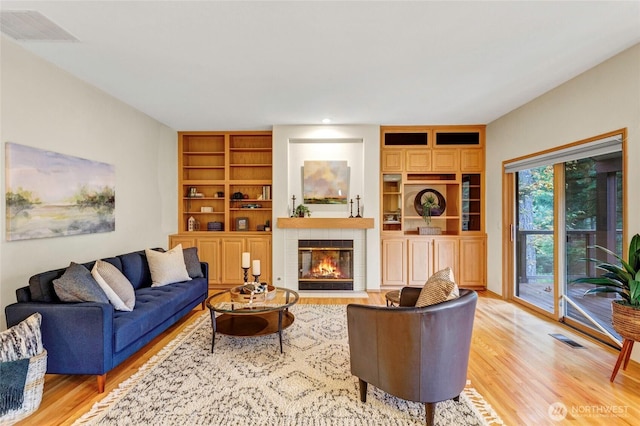 living area featuring built in shelves, a tiled fireplace, visible vents, and light wood-style floors