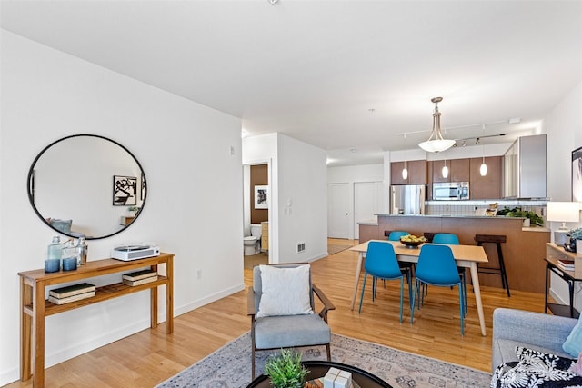 living area featuring light wood finished floors, track lighting, visible vents, and baseboards