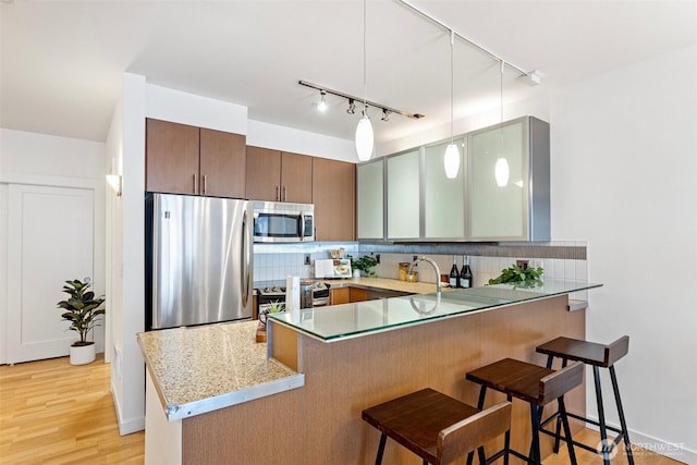 kitchen with a breakfast bar area, a peninsula, appliances with stainless steel finishes, light wood-type flooring, and tasteful backsplash