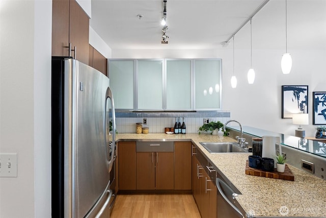 kitchen with light wood finished floors, stainless steel appliances, decorative backsplash, a sink, and a peninsula