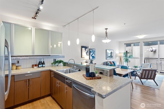 kitchen with stainless steel appliances, backsplash, light wood-style floors, a sink, and a peninsula