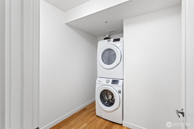 clothes washing area with baseboards, laundry area, light wood-style flooring, and stacked washer / drying machine