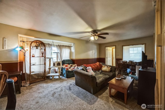 living area featuring a wealth of natural light, wainscoting, carpet flooring, and ceiling fan