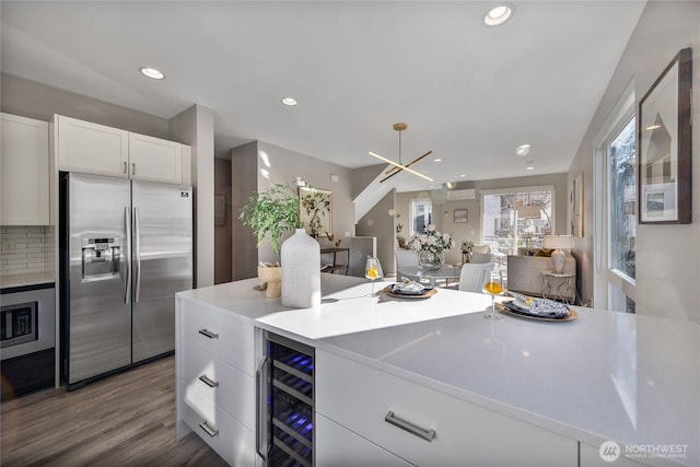 kitchen with hardwood / wood-style flooring, stainless steel appliances, beverage cooler, decorative backsplash, and white cabinets