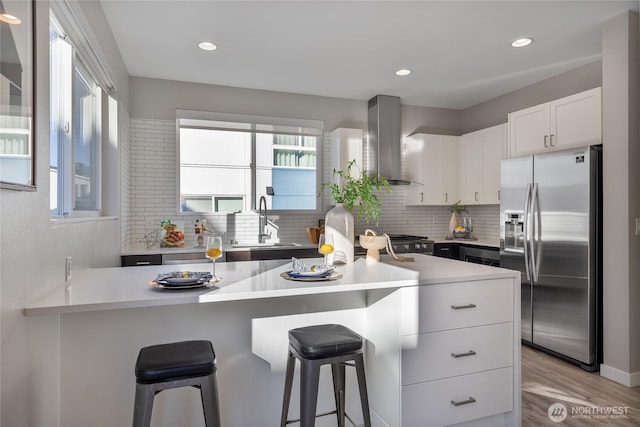 kitchen featuring white cabinetry, stainless steel fridge, a kitchen breakfast bar, and exhaust hood