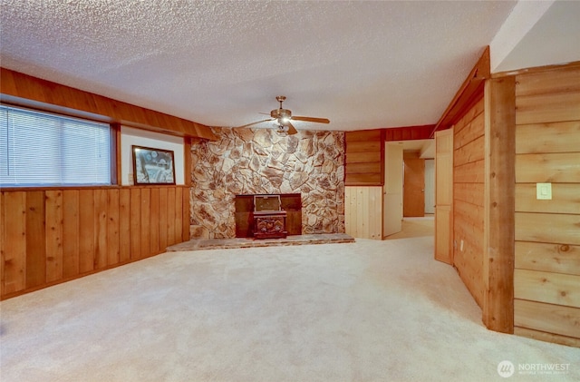 unfurnished living room featuring ceiling fan, carpet, a textured ceiling, and wood walls