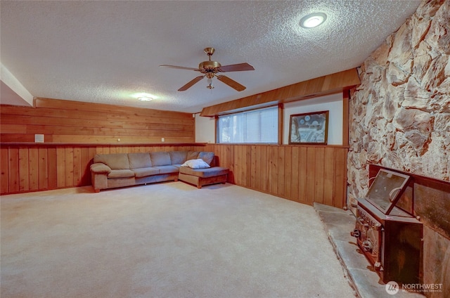 unfurnished living room with ceiling fan, wooden walls, light colored carpet, and a textured ceiling