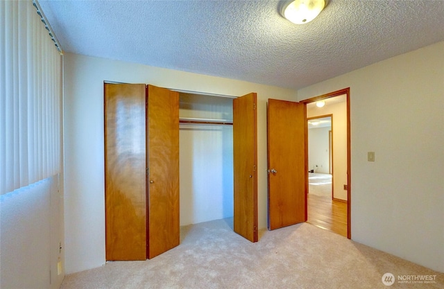 unfurnished bedroom featuring light carpet, a textured ceiling, and a closet