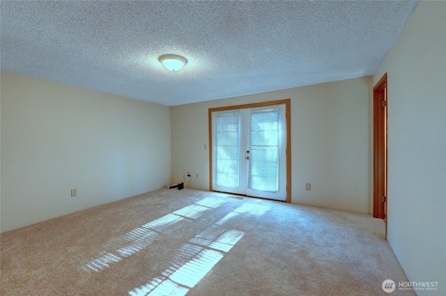 spare room with light carpet, a textured ceiling, and french doors