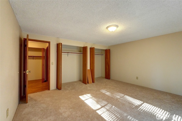 unfurnished bedroom featuring light colored carpet, a textured ceiling, and two closets