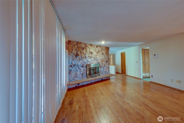 unfurnished living room with a stone fireplace and light wood-type flooring