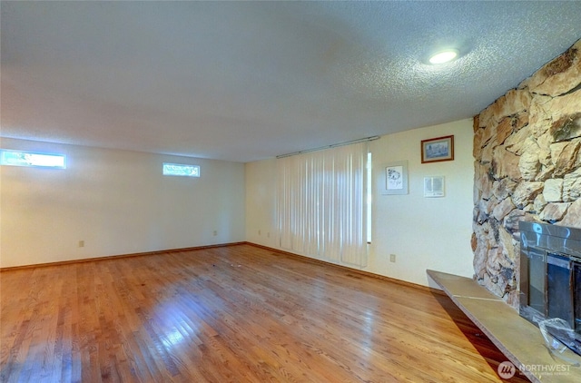 unfurnished living room featuring a stone fireplace, light hardwood / wood-style floors, and a textured ceiling