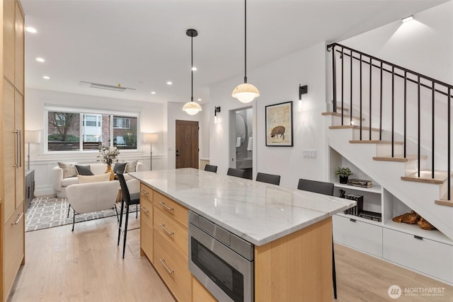 kitchen with modern cabinets, stainless steel microwave, open floor plan, a breakfast bar area, and light brown cabinets