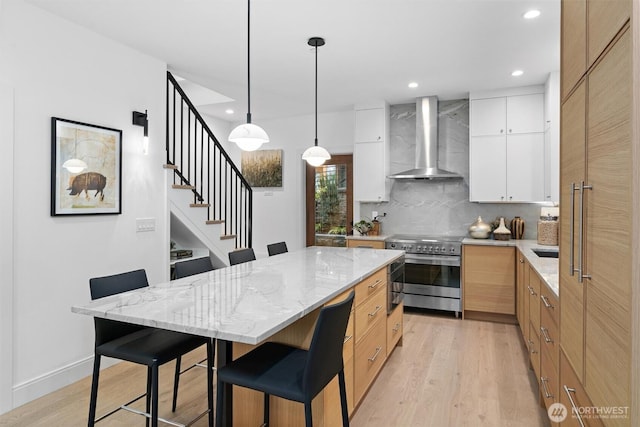 kitchen with a center island, white cabinets, light stone countertops, high end stove, and wall chimney range hood