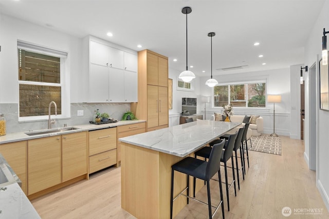 kitchen with a sink, light wood-style floors, decorative backsplash, light brown cabinetry, and a kitchen bar