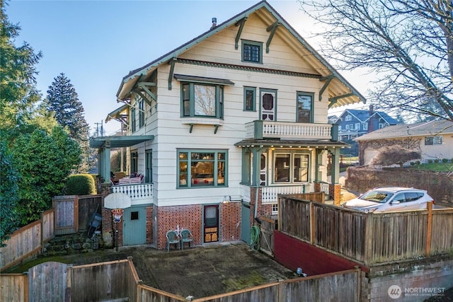 back of house featuring a balcony, a fenced backyard, and brick siding