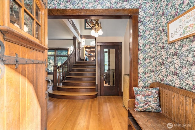 staircase with wallpapered walls, wood finished floors, and a chandelier