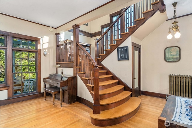 stairs with radiator, wood finished floors, baseboards, and ornate columns