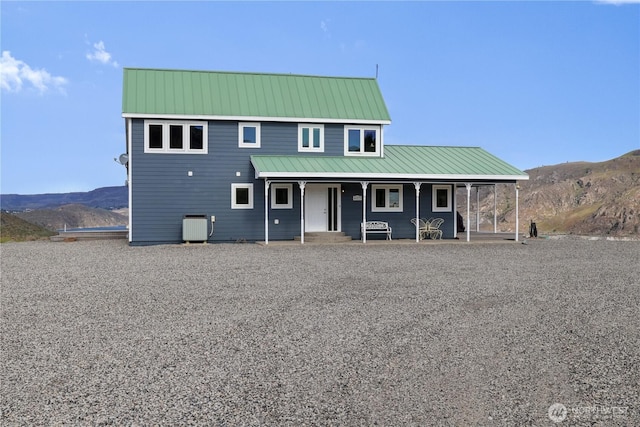 farmhouse inspired home featuring a mountain view, central air condition unit, covered porch, and metal roof