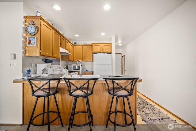 kitchen with sink, white appliances, a breakfast bar area, and kitchen peninsula