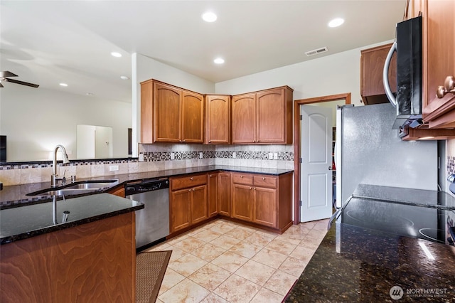 kitchen with appliances with stainless steel finishes, sink, tasteful backsplash, and dark stone counters