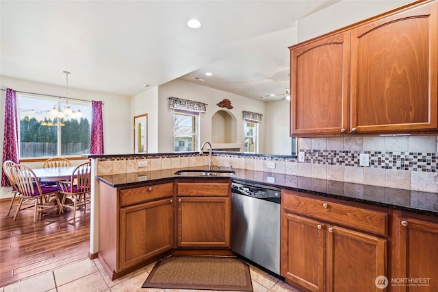 kitchen featuring stainless steel dishwasher, pendant lighting, backsplash, sink, and dark stone countertops