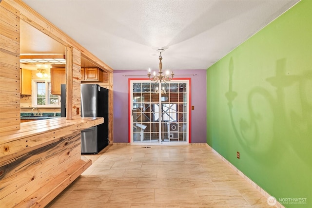 kitchen with sink, a chandelier, hanging light fixtures, a textured ceiling, and stainless steel refrigerator