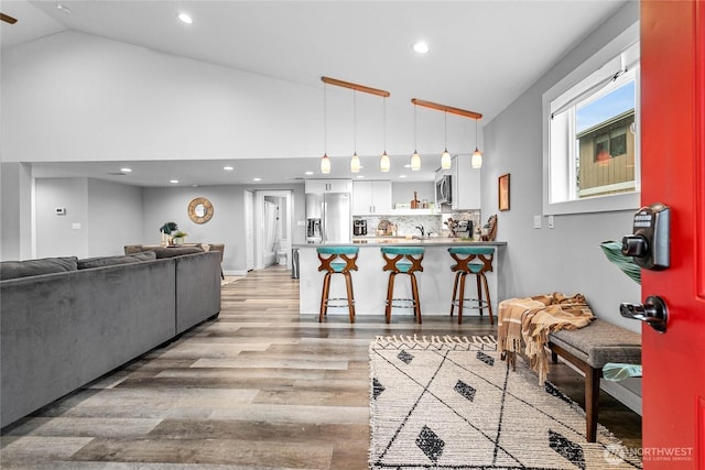 living room featuring high vaulted ceiling, wet bar, and light hardwood / wood-style floors