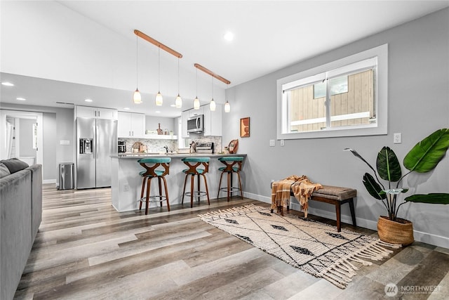 kitchen featuring kitchen peninsula, hanging light fixtures, a breakfast bar, appliances with stainless steel finishes, and white cabinets