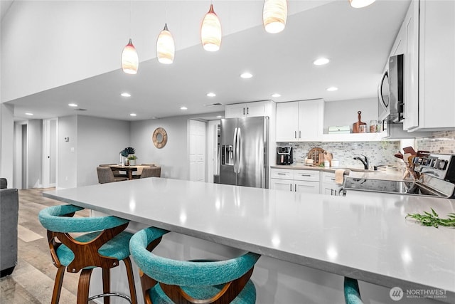 kitchen featuring appliances with stainless steel finishes, hanging light fixtures, white cabinets, and backsplash