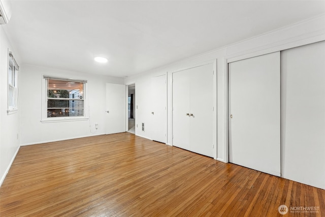 unfurnished bedroom with wood-type flooring, a wall mounted AC, and multiple closets