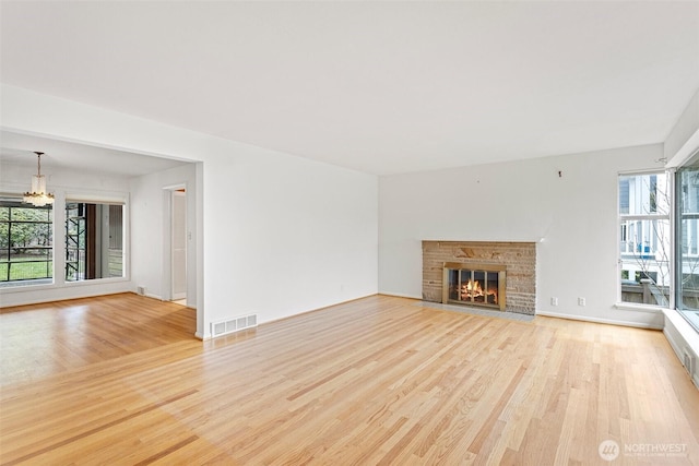 unfurnished living room with a notable chandelier, light hardwood / wood-style floors, and a wealth of natural light