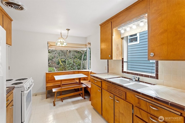 kitchen featuring tile countertops, white range with electric stovetop, sink, decorative backsplash, and hanging light fixtures