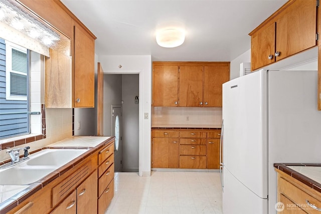 kitchen with tasteful backsplash, sink, tile countertops, and white refrigerator