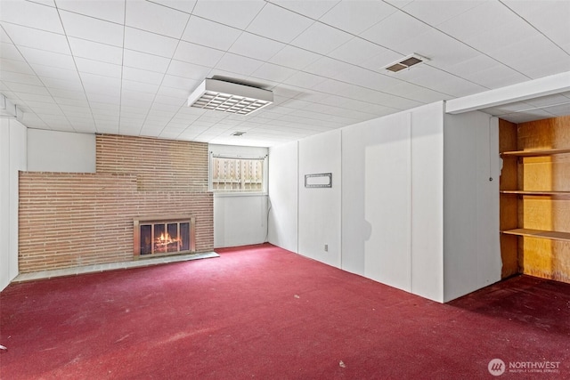 basement featuring a brick fireplace, dark carpet, and brick wall