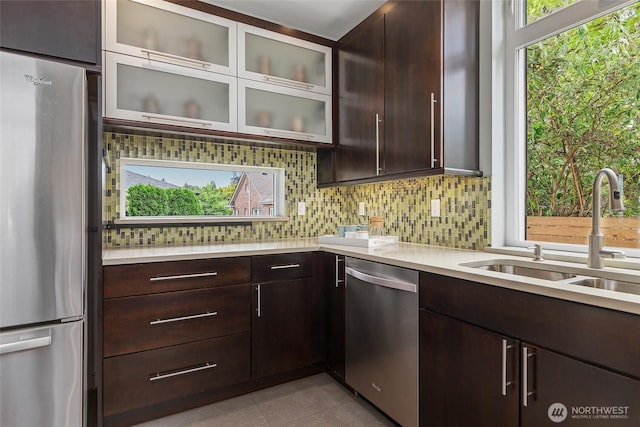 kitchen with tasteful backsplash, glass insert cabinets, stainless steel appliances, light countertops, and a sink